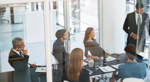 foto de um grupo de pessoas dentro de uma sala de escritório com paredes de vidro.
